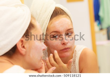 Woman applying mask moisturizing skin cream on face looking in bathroom mirror. Girl taking care of her complexion layering moisturizer. Skincare spa treatment. 