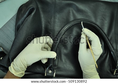 A leather factory worker coloring a black leather bag at the finishing line. The hands of the worker covered with gloves and applying paint on the lather beg with a brush.  Royalty-Free Stock Photo #509130892
