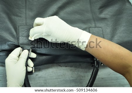 A leather factory worker cleaning a black leather bag with cleaning cloth. The hands of the worker covered with gloves and rubbing the lather beg with a microfiber cotton cloth.  Royalty-Free Stock Photo #509134606