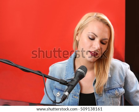 Young woman playing piano and singing in recording studio