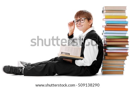 Cute schoolboy sitting beside heap of books on white background