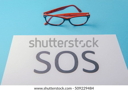 Word SOS written on white paper. Blue background