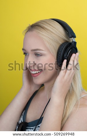 Young woman with headphones listening music and having funn. Blond feeling happy against yellow background