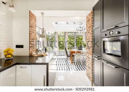 Bright kitchen area with modern amenities, close brick walls with the view of minimalistic dining room surrounded by windows Royalty-Free Stock Photo #509293981