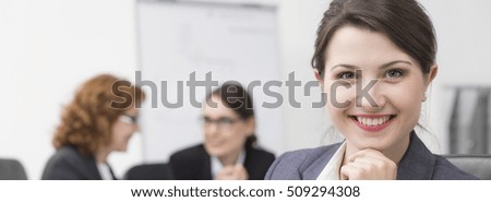 Panoramic picture of a young smiling businesswoman looking at the camera and her two friends talking in the background