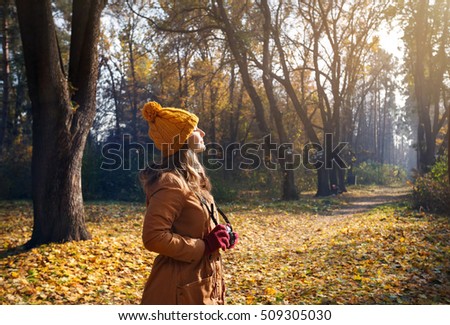 Woman in brown jacket and yellow hat taking a picture with old vintage photo camera at autumn forest 