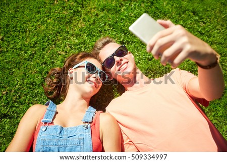 love and people concept - happy teenage couple in sunglasses lying on grass and taking selfie on smartphone at summer