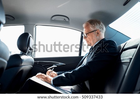 transport, business trip, paperwork and people concept - senior businessman signing papers with pen and driving on car back seat