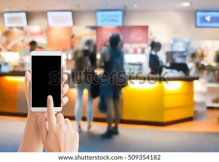 woman use mobile phone and blurred image of people order their food at the counter of fast food shop , coffee shop