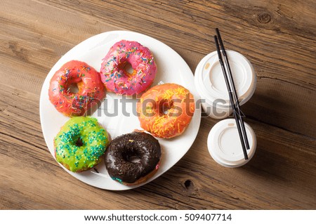 Multi-colored glazed donuts. On a white plate, on wooden boards. Coffee to donuts
