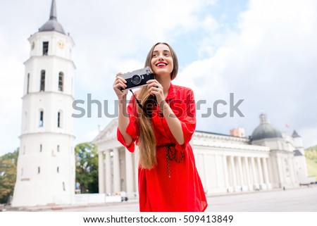 Portrait of a young female tourist with photo camera on the cathedral square in front of the famous basilica in Vilnius. Woman having great vacations in Lithuania