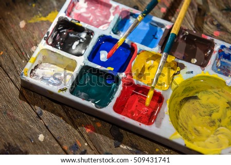 colorful colors palette and paint brushes on dirty wooden artist table