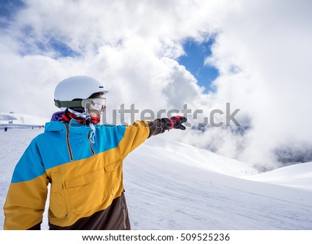 Portrait of woman snowboarder pointing way on background beautiful landscape of snowy high mountains of Caucasus at Krasnaya Polyana, standing with snowboard