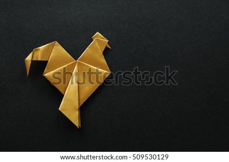 Golden shiny paper folded rooster handmade origami craft on black background. Nice natural holiday greeting card template. Empty space for text, copy, lettering.
