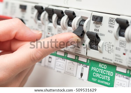An RCD circuit breaker board displays many switches. Most are in the ON position, but one is switched down to OFF. It is the circuit for the lighting. A finger is about to turn it back on Royalty-Free Stock Photo #509531629