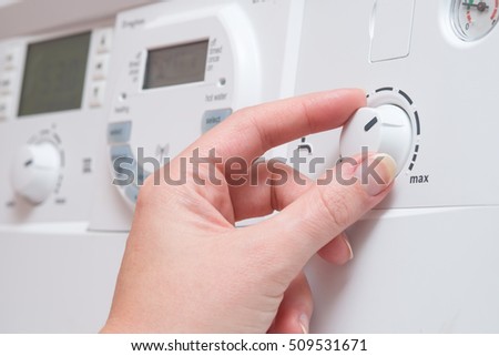 A hand adjust the dial controlling water temperature on a white boiler. It appears to be turning towards the MAX setting.  Other buttons and a digital display are visible in the background Royalty-Free Stock Photo #509531671