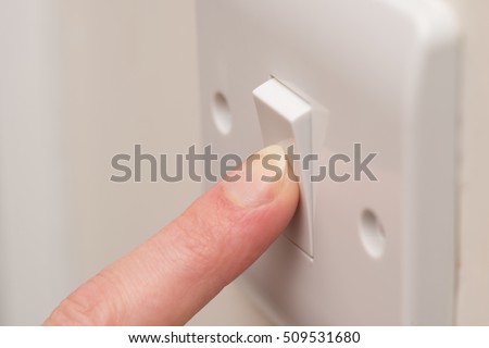 Close up. A finger presses down on a single white light switch on a cream wall. COPY SPACE Royalty-Free Stock Photo #509531680