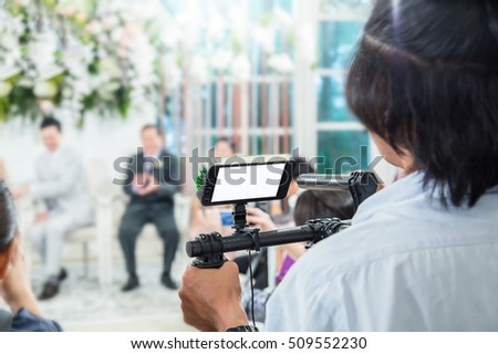 Videographer takes video camera with blank screen and blur image of group people in the background with free copy space for your text