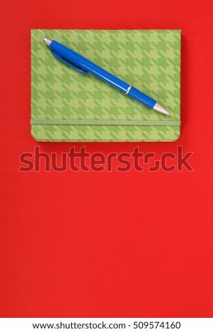 Green closed notebook with blue pen isolated on red background with soft shadow, place for your text