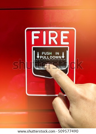 a hand reaching and pulling a red fire alarm switch. red fire alarm. Push in pull down.
