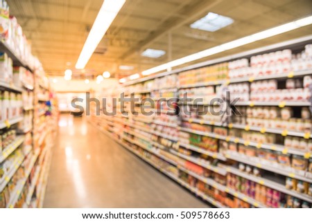 Blurred image of condiment, soup, pasta and canned vegetable aisle in store. Wide perspective view aisle, shelves with variety of products, defocused blurry background with bokeh light in supermarket.