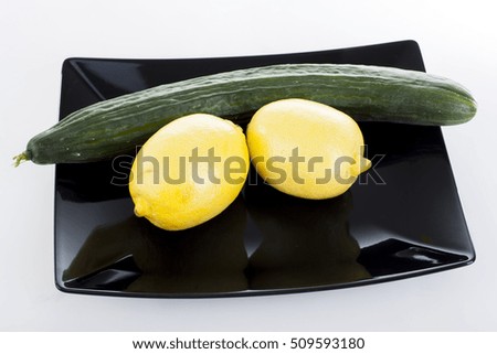 cucumber and lemons on black plate.