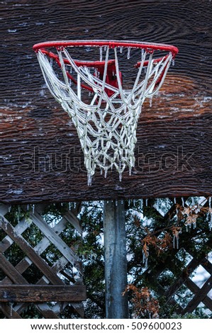 Basketball net encased in ice after a storm. Ice storm in Toronto, frozen water droplets on surfaces. Beautiful wooden background, shallow depth of field. Icicles on sports court and net.