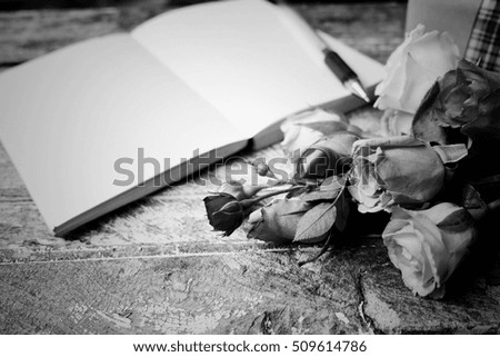 Rose and notebook on wooden table black and white tone.