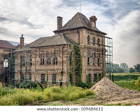 Picture of the old abandoned mansion-house with wooden trestle for alteration work. Verdurous mansion against the background of cloudy sky.