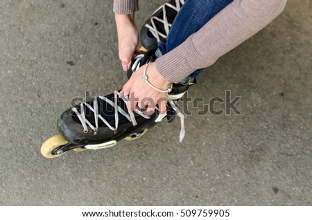 Young girl ties shoelaces on black rollers in the park