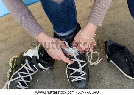 Young girl ties shoelaces on black rollers in the park