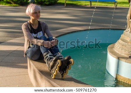 Young girl sitting near the fountain and wearing black rollers in the park 