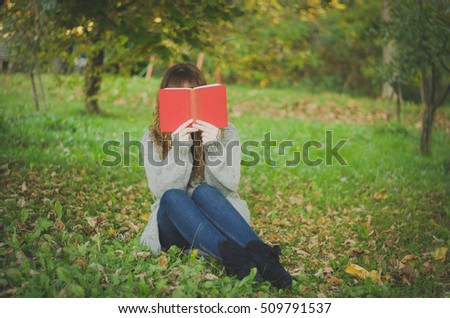 Girl reading book sitting in the park in autumn