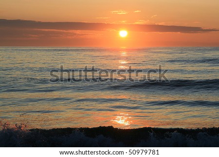 Sunrise is pink. Sun is yellow in orange sky and clouds under wave of sea.