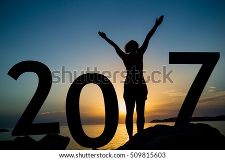 Happy new 2017 year card. A girl standing on a rocky shore, watching the sunset, standing as a part of 2017 sign