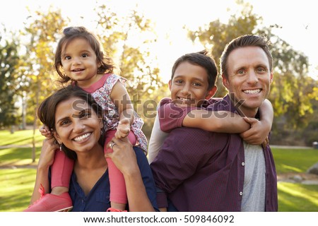 Mixed race parents carry their kids piggyback in a park Royalty-Free Stock Photo #509846092