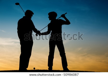Mature or senior couple playing golf - pictured as a silhouette against an evening sky