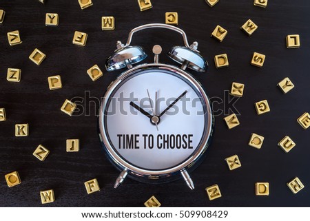 Time to choose - Alarm clock on wooden table with letters
