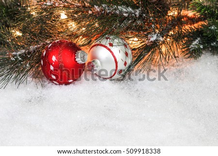Christmas background with red and silver ornaments,  string of lights and Christmas tree garland border in snow; white copy space background