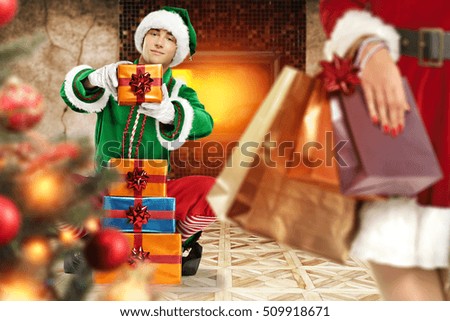 green elf in room with fireplace and xmas tree and santa claus woman hand with few gifts 