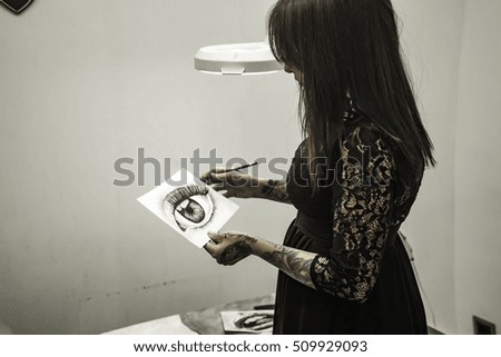 Portrait tattooed woman artist showing her charcoal drawing in studio.