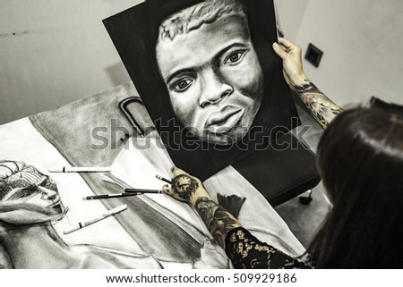 Portrait tattooed woman artist showing her charcoal drawing in studio. High angle
