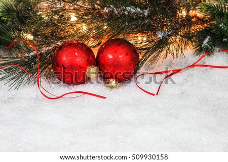 Christmas background with red and gold ornaments, string of lights and Christmas tree garland border in snow; white copy space background 