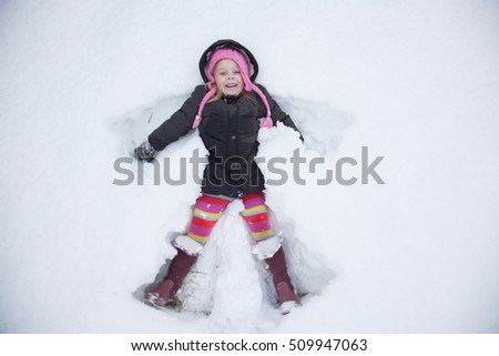 Light hair girl in pink hat play with snow, make snow angel. Royalty-Free Stock Photo #509947063