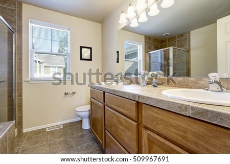 Bathroom interior in beige and brown colors. Wooden double sink vanity cabinet with large mirror, toilet and shower. Northwest, USA