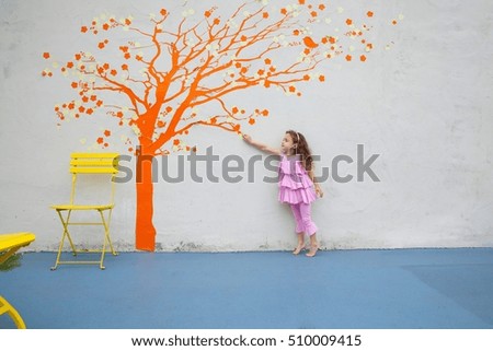 Girl pointing to orange tree mural on wall