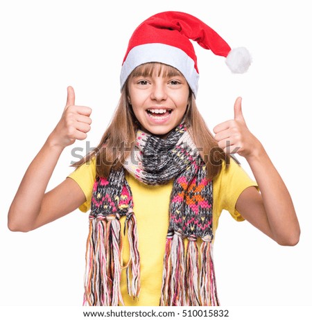 Half-length portrait of caucasian girl wearing Santa Claus hat. Schoolgirl looking at camera and making thumbs up gesture. Holiday Christmas concept - happy cute child isolated on white background.