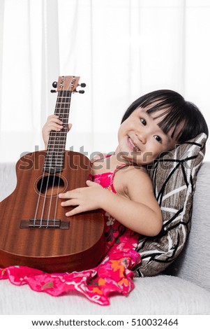 Happy Asian Chinese little girl sitting on the sofa playing ukele