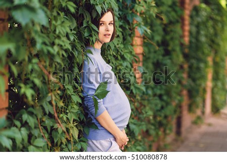 Pregnant woman leaning against a wall of green plants