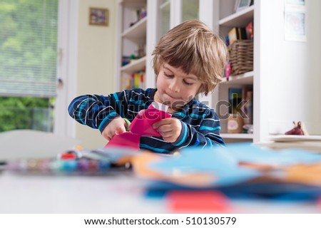 Cute little boy cutting shapes out of colored paper. Children being creative, developing imagination, creativity, do it yourself concept
